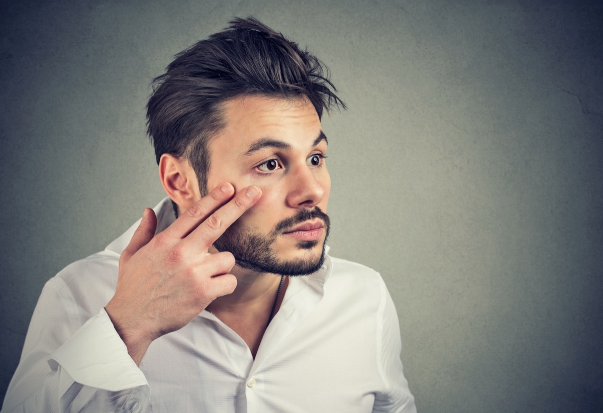 young man pulling down eyelid to check eye in mirror