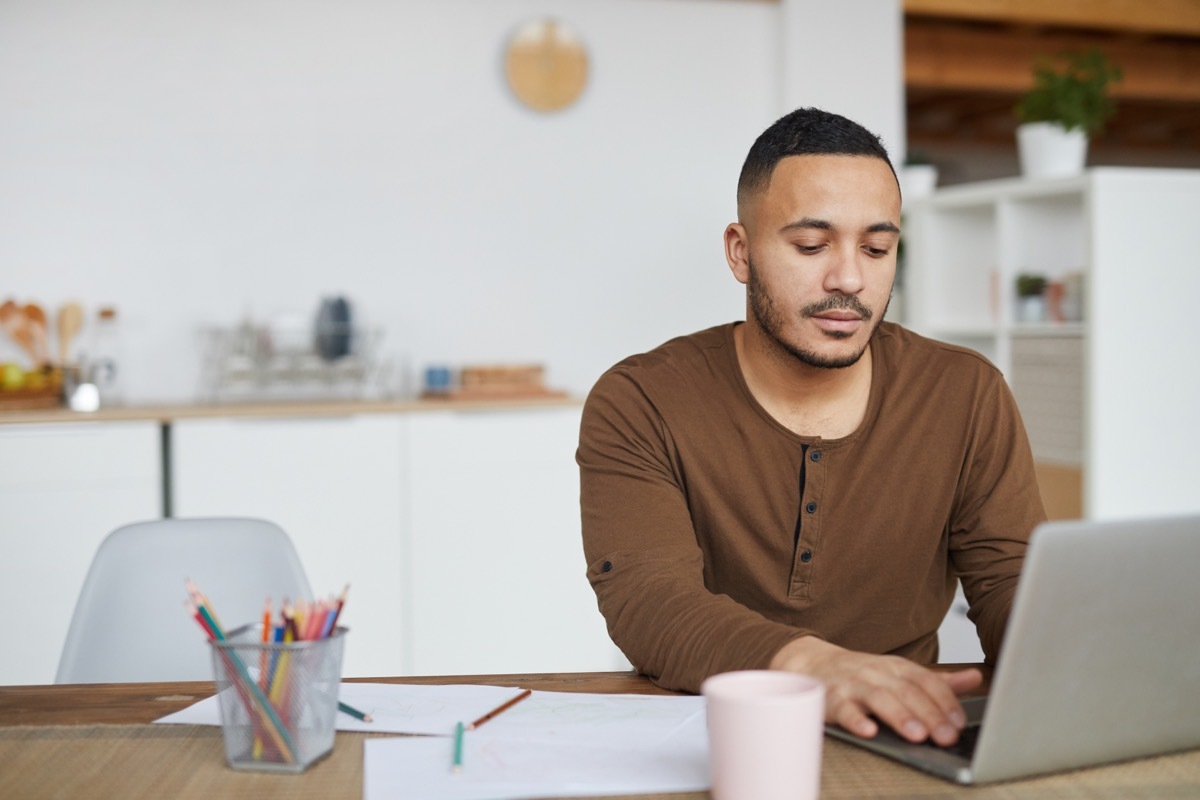 Portrait of man using laptop while working in home interior, copy space