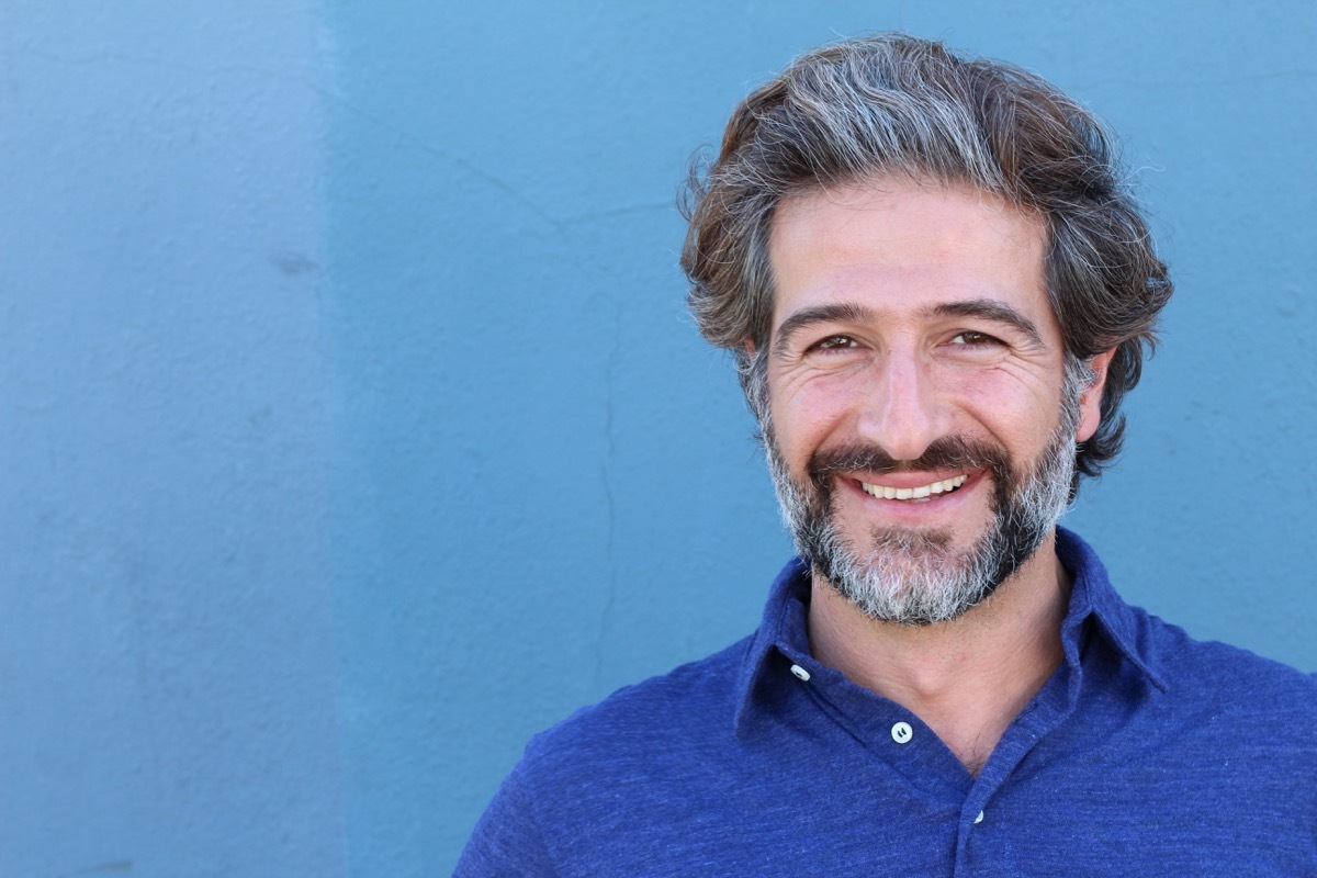 man with a gray beard and gray hair and a blue polo against a blue background