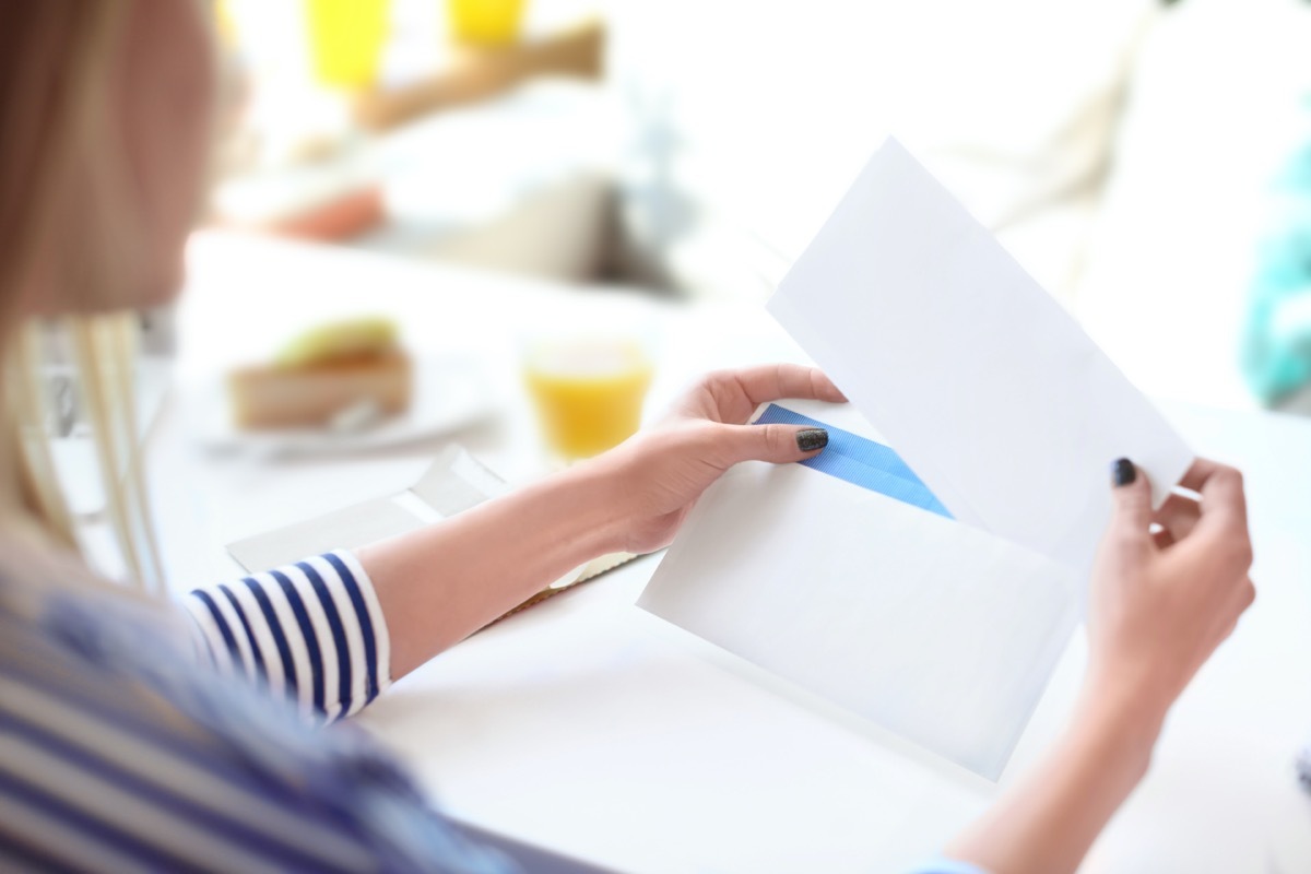 Young woman putting letter into envelope at table in cafe. Mail delivery