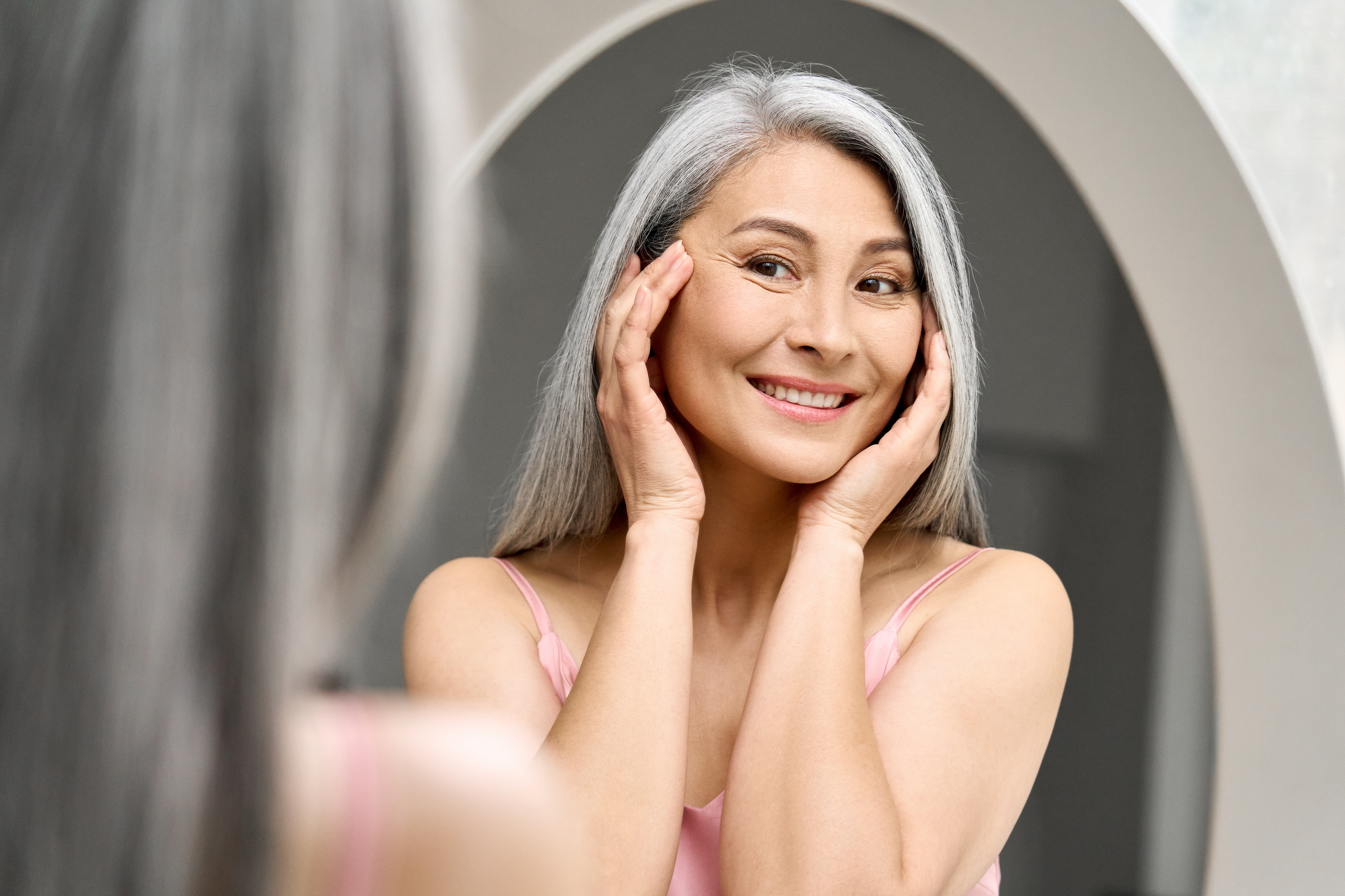 Happy senior asian woman looking at her face and smiling