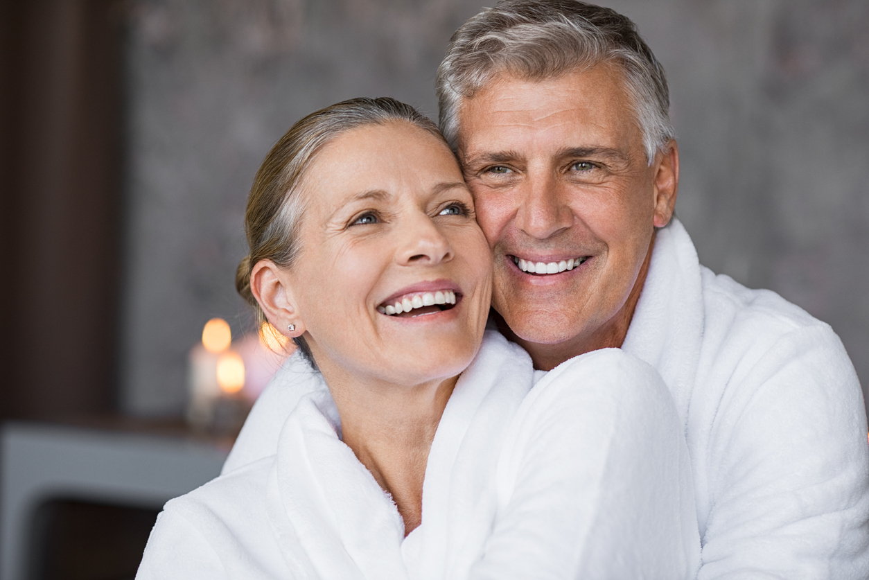 An older heterosexual couple hugging while wearing robes