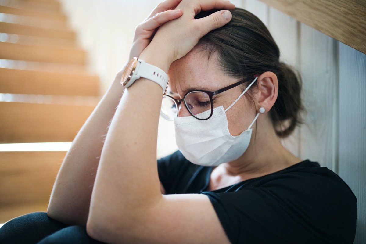 Sad woman with face mask sitting indoors at home,