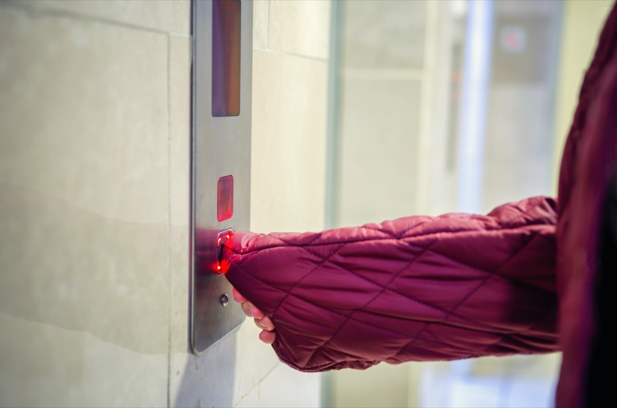 A woman pushing an elevator button with sleeve nylon down jacket instead of using her hand.