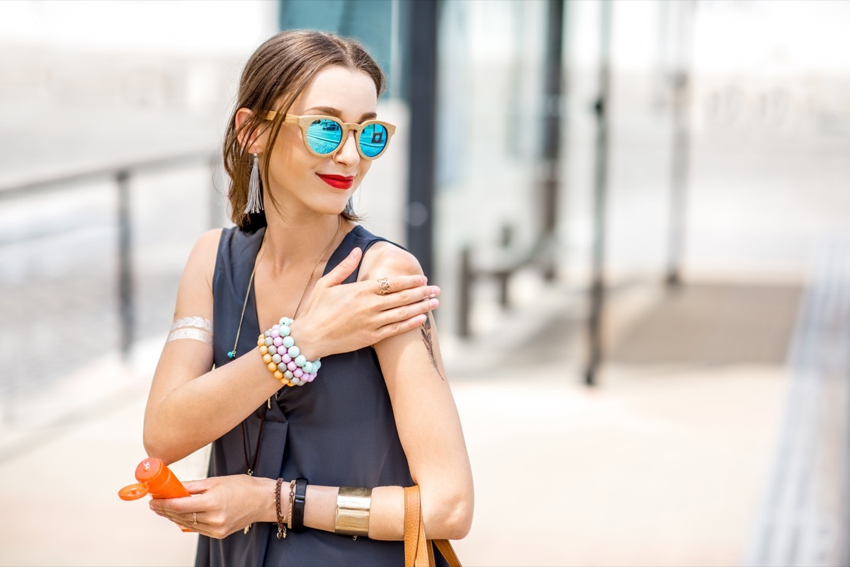 woman applying sunscreen lotion standing outdoors at the urban location during the sunny weather