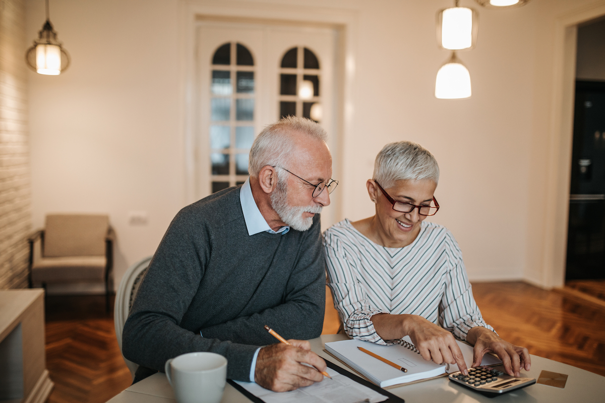 A happy senior couple calculating their finances in a beautiful home.