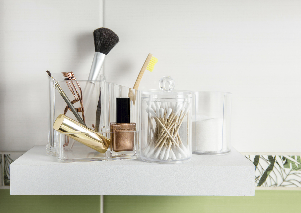 Cotton pads, Q-tips, make up brushes, and more beauty products in organizer container boxes on tidy shelf in bathroom