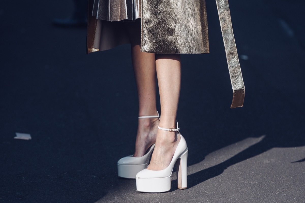 Street style, woman wearing a beige and brown accordion halter-neck short dress, brown shiny leather handbag, white varnished leather platform sole high heels shoes.