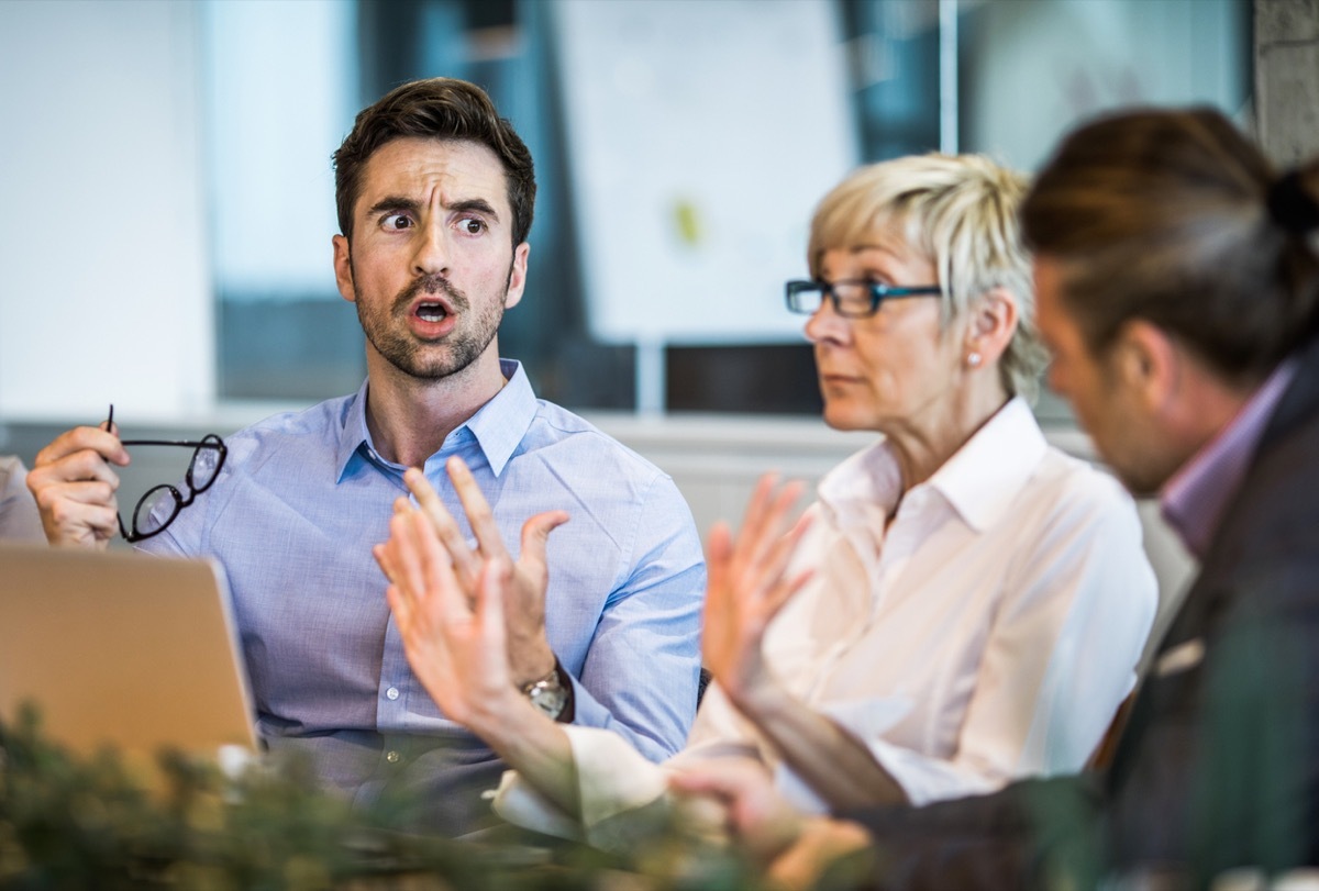 white man looking shocked at work next to older white woman putting up her hands