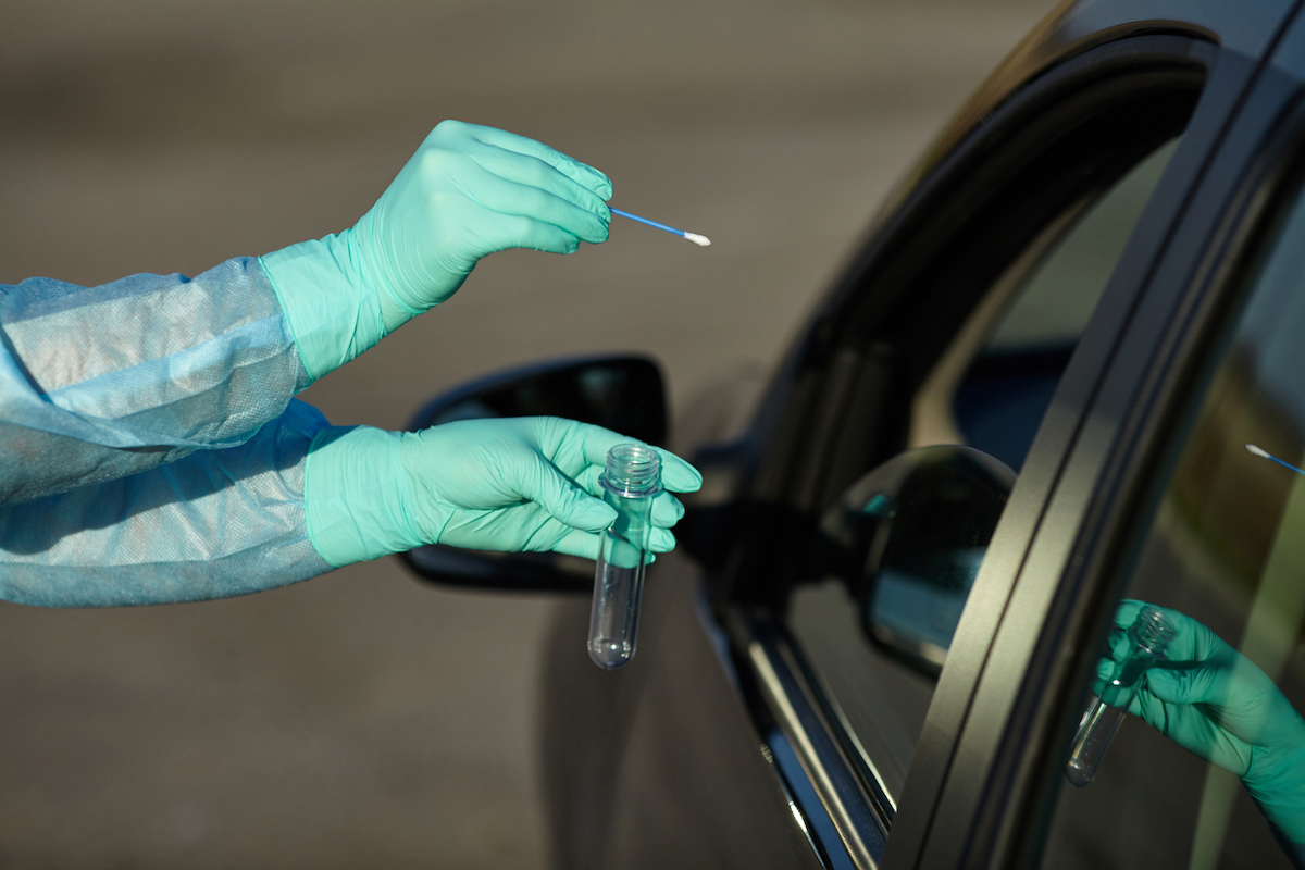 Medical worker in full protective gear takes sample from patient at a COVID-19 drive-thru test site