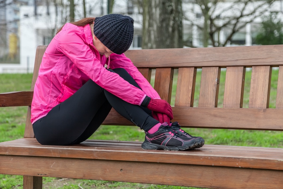 Young athlete woman tired or depressed resting on a bench on a cold winter day in the track of an urban park.