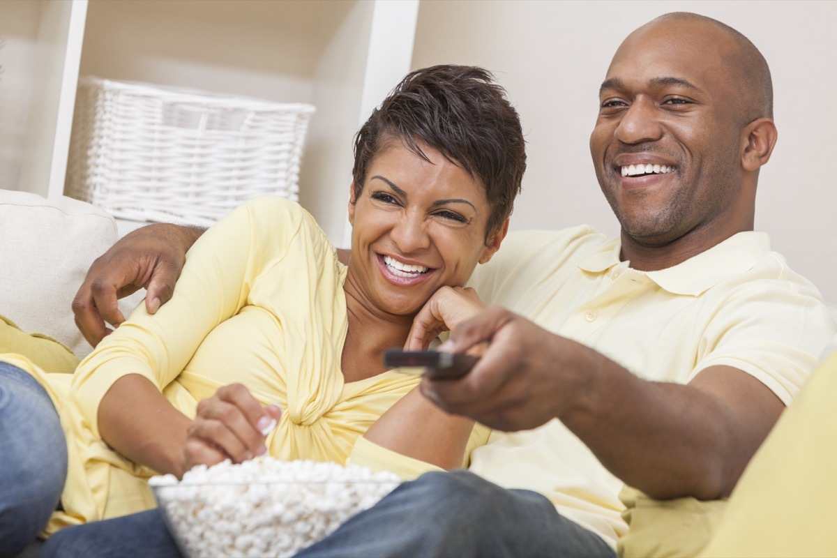 Black couple watching television with a remote on the couch