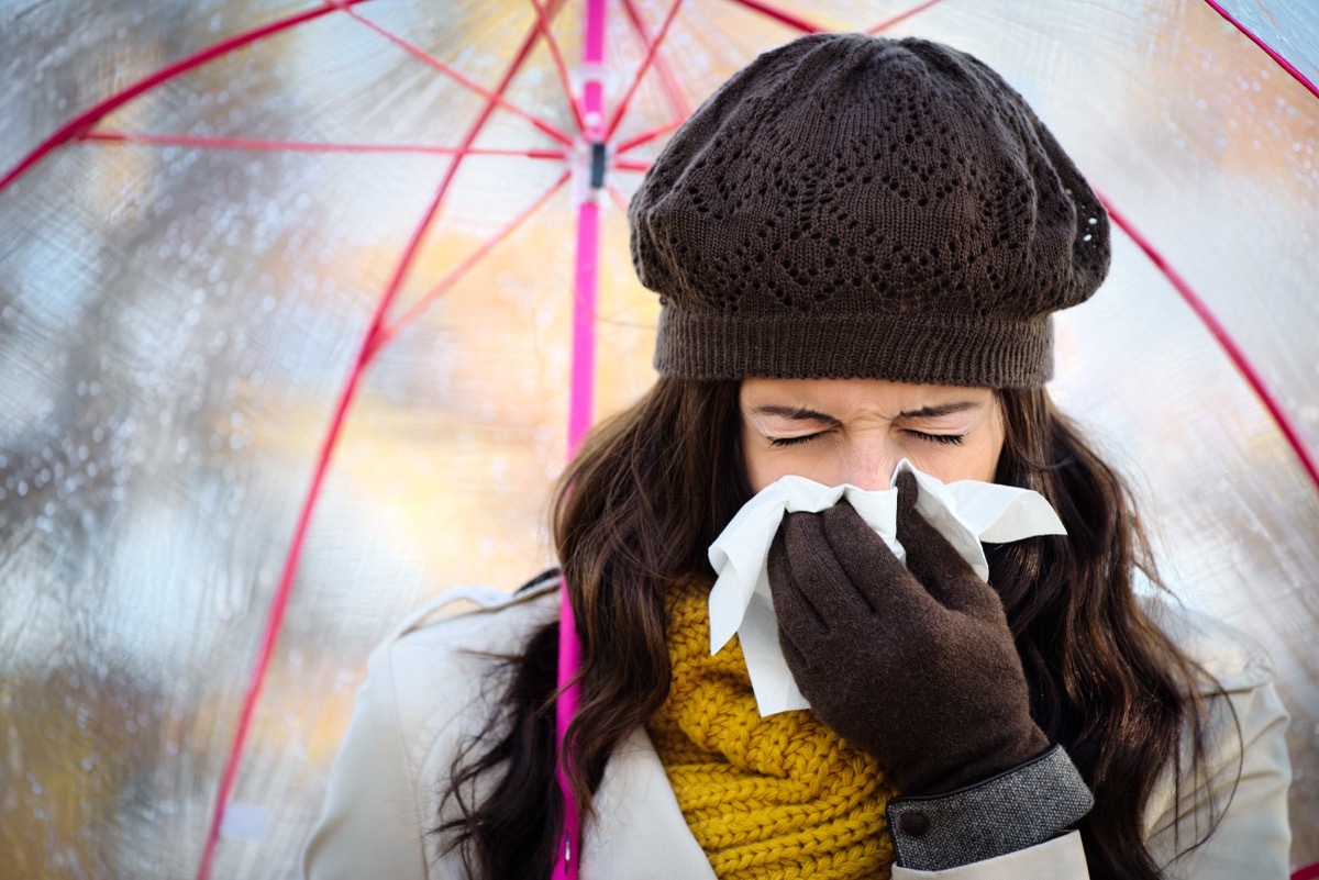 woman sneezing while holding an umbrella in cold weather