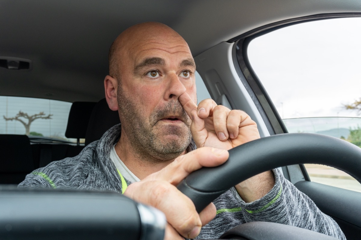 Middle aged man picking his nose driving a car.