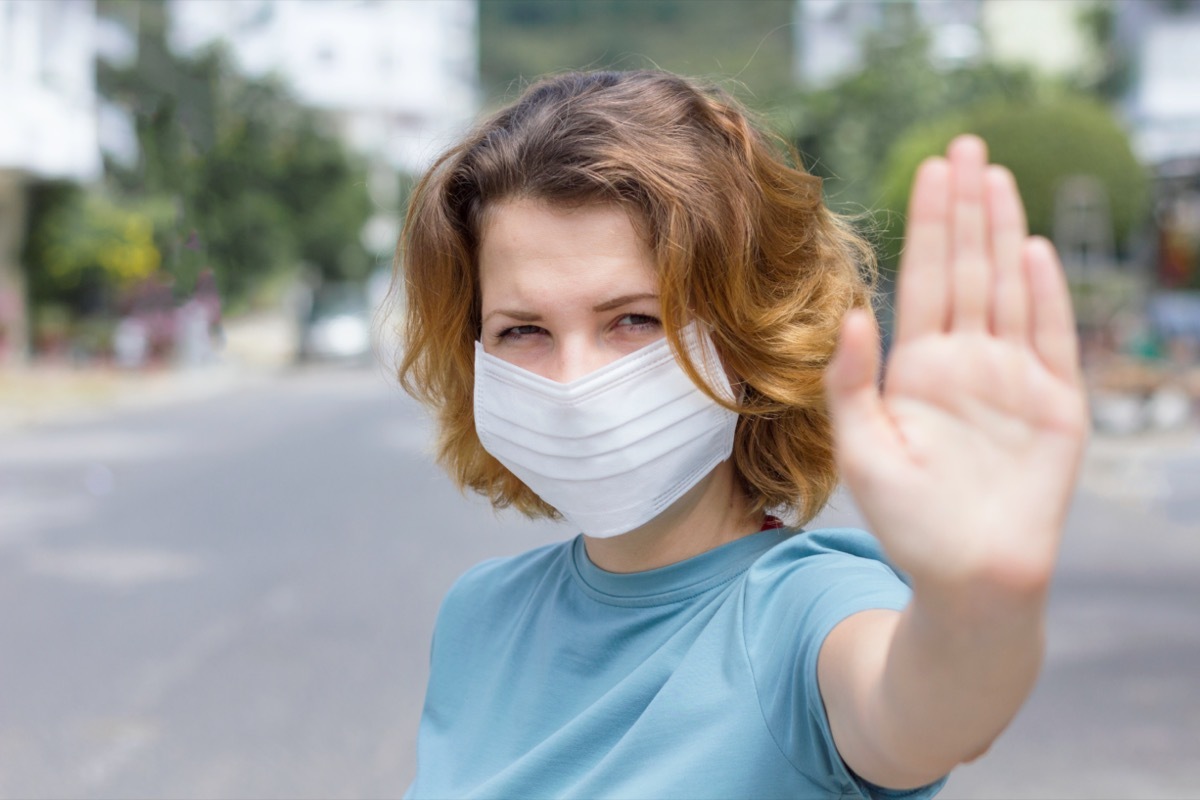 woman in protective sterile medical mask on her face looking at camera outdoors, on asian street show palm, hand, stop no sign