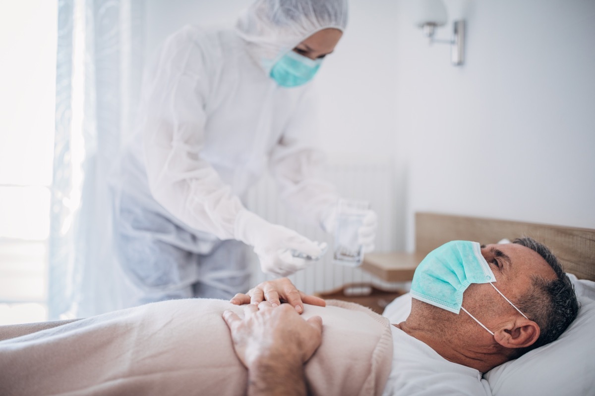 Man and woman, senior man lying in hospital bed because of coronavirus infection, female doctor is giving medicine to a patient.