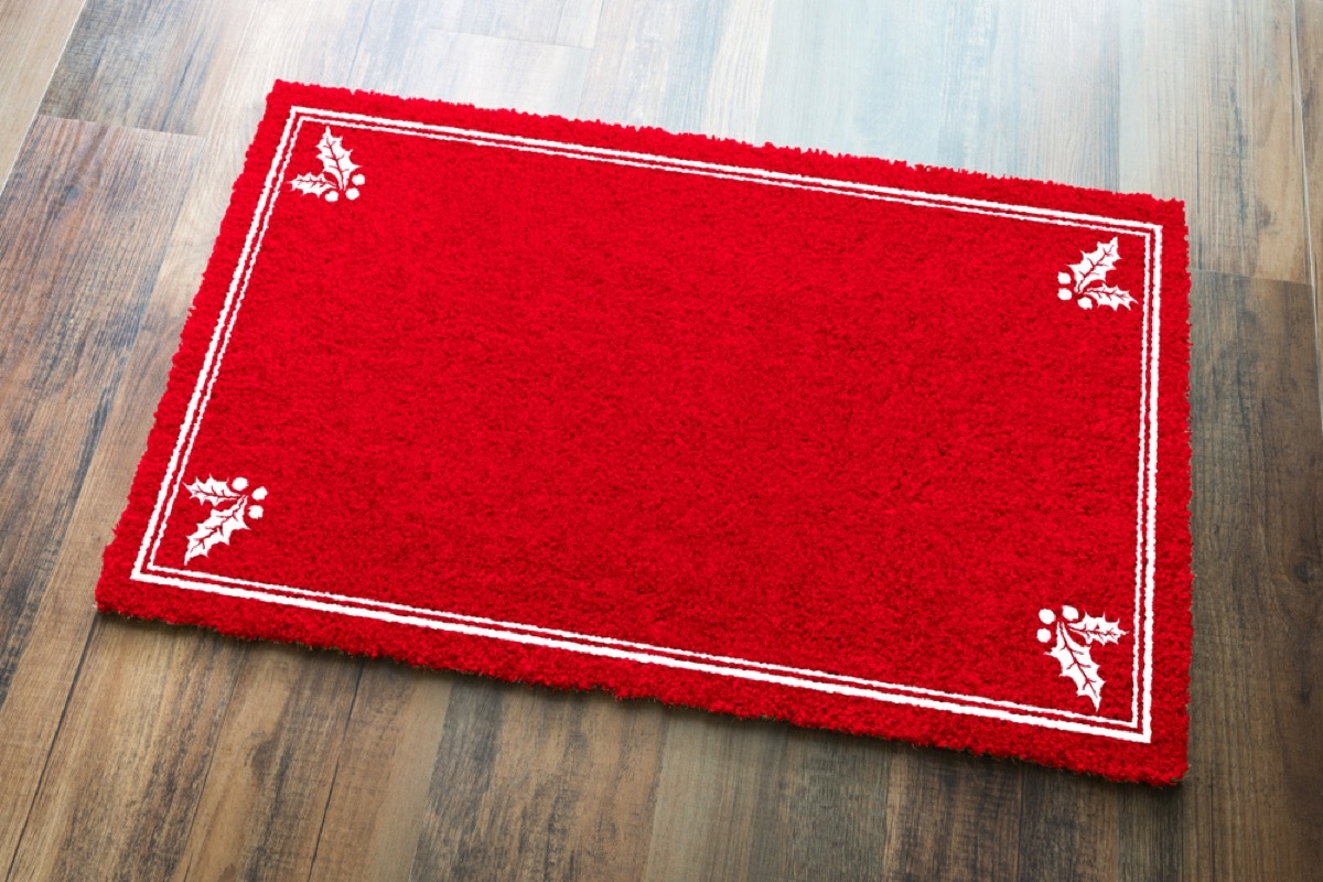 red welcome mat on wood floor with white holly leaves in corners