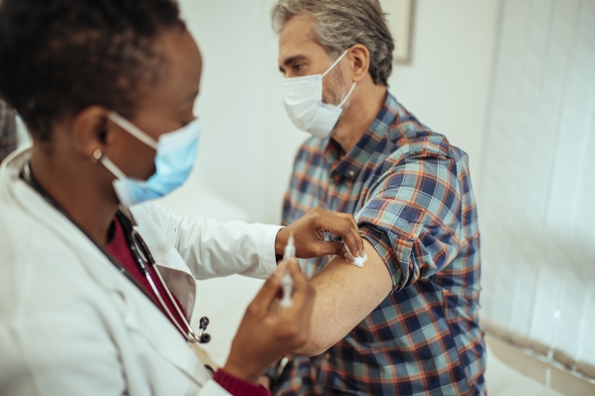 doctor giving flu or covid19 vaccine to a middle-aged man wearing protective face masks. Vaccination and prevention against virus pandemic.