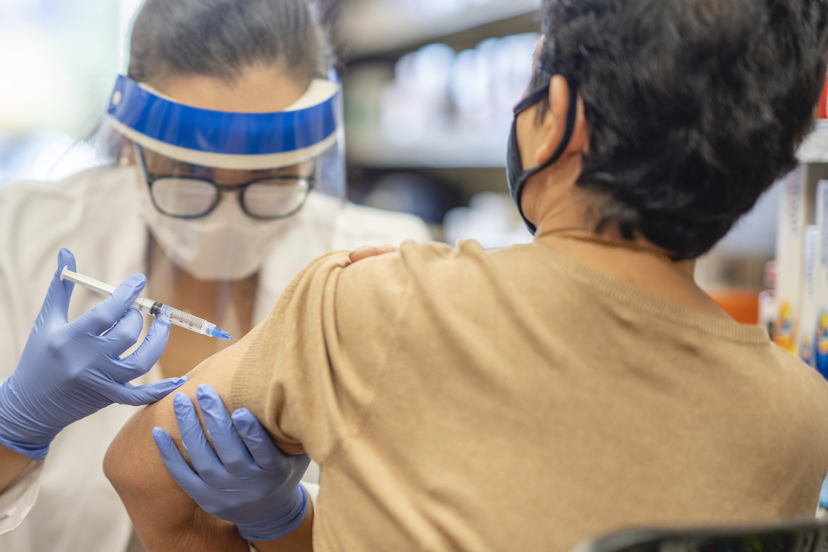 Masked senior getting a vaccine while at the pharmacy by a female pharmacist.