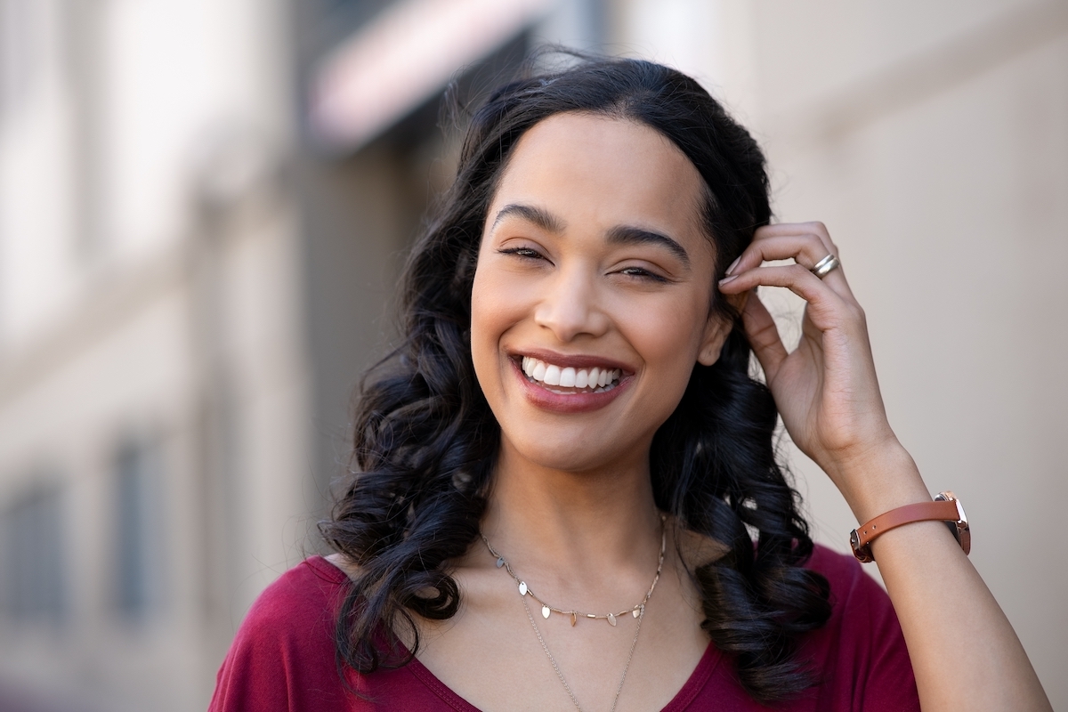 A pretty young woman with black hair on a city street wearing burgundy red lipstick and shirt