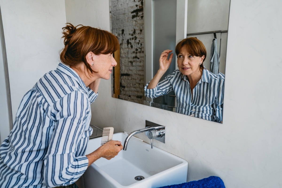 Senior woman adjusting her hair in front of a mirror in bathroom.