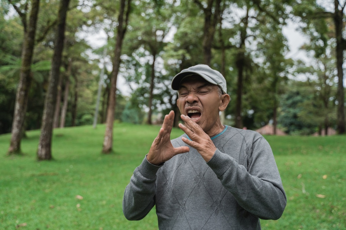 South Asian man sneezes in park without covering mouth, etiquette over 40