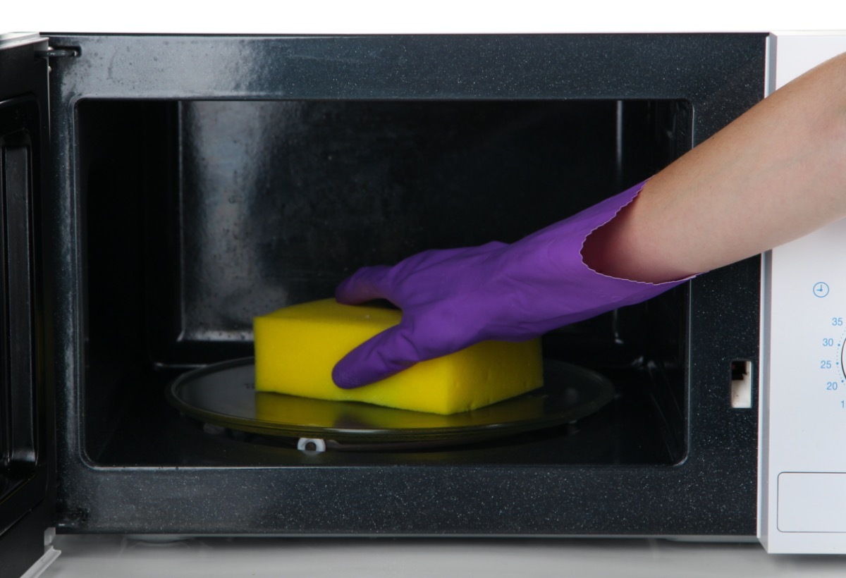 Hand with sponge cleaning microwave oven.