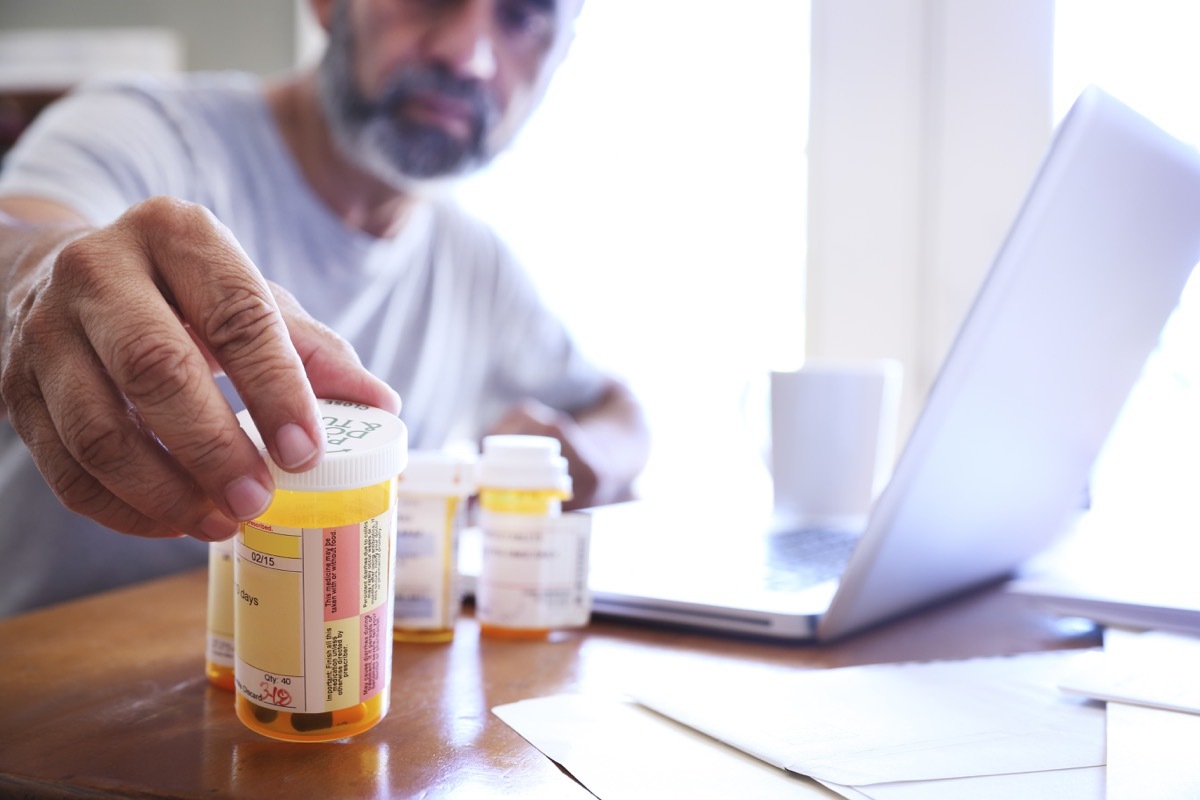 man in his late fifties reaches for one of his prescription medication bottles as he sits at his dining room table