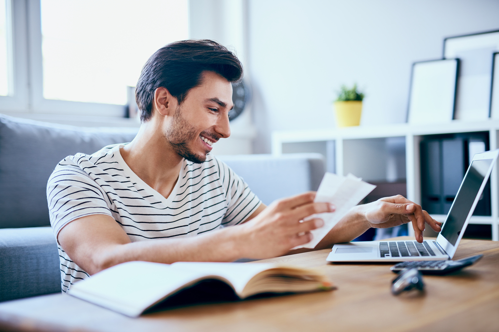 A young man filing taxes on his laptop while smiling and maybe cashing his COVID stimulus check