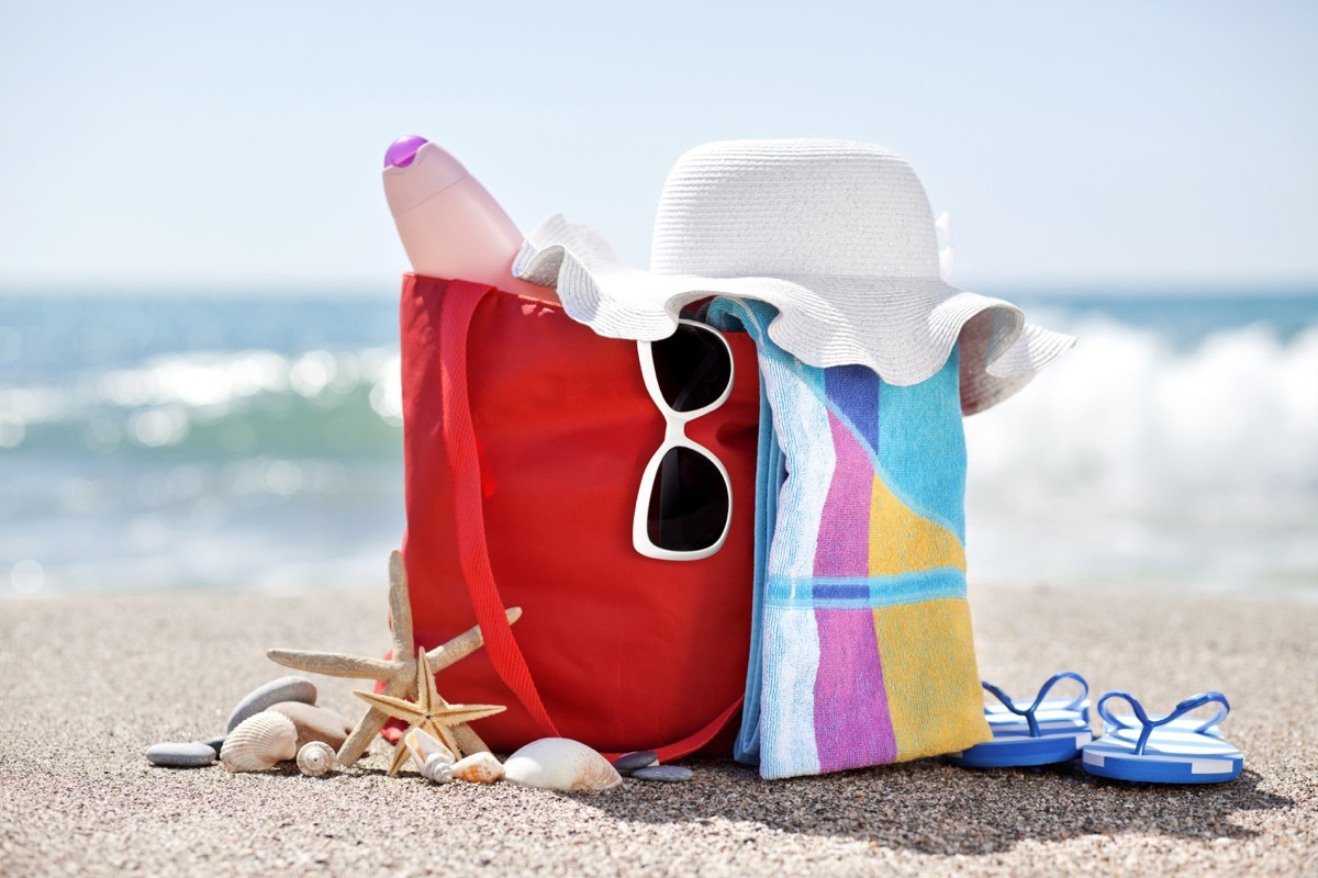 beach bag with hat,towel, sunglasses, sun lotion, pebbles, seashells and flip flops at the beach