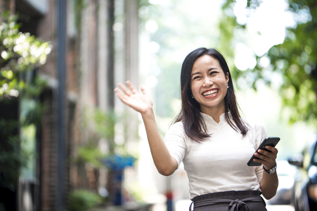 Portrait of a friendly woman on the street waving at someone with a big smile on her face