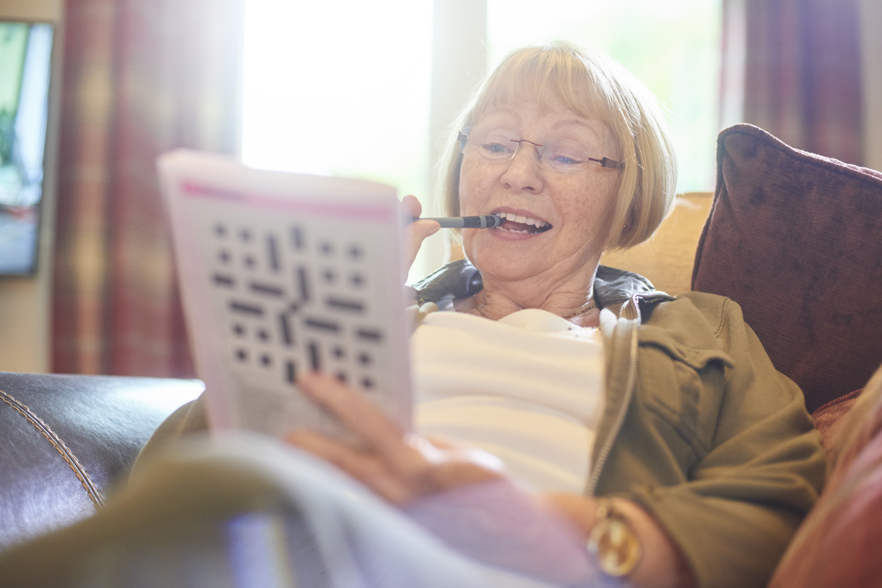 Senior woman doing crossword puzzle at home. 