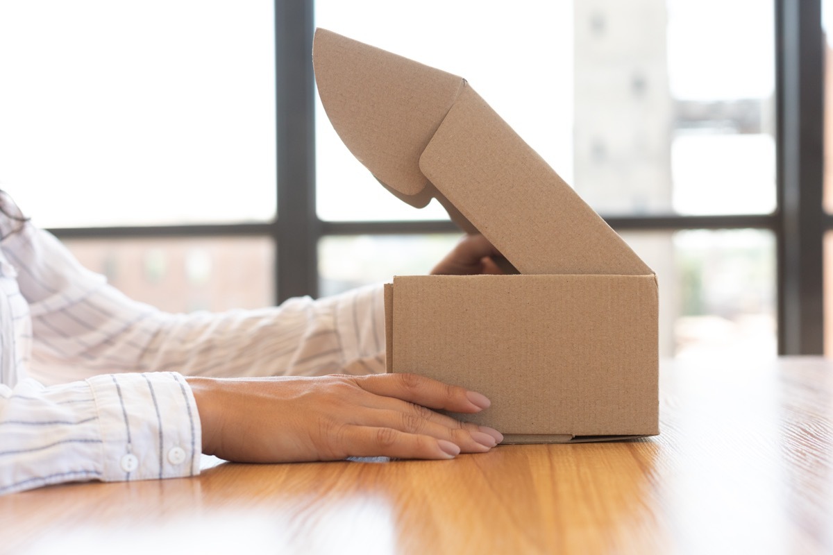 Female hands lifting lid of cardboard package on wooden table