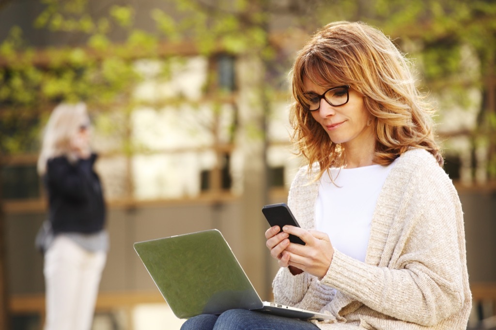 woman working on smartphone and laptop computer outside