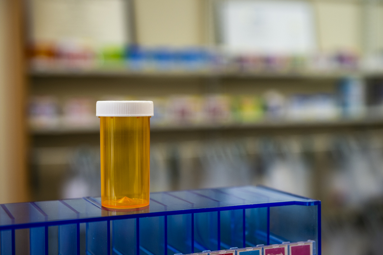 An empty prescription bottle standing on a blue case in a pharmacy