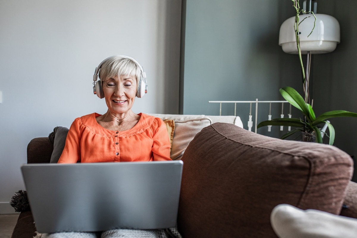 Happy senior woman, lying on the couch and looking at the laptop