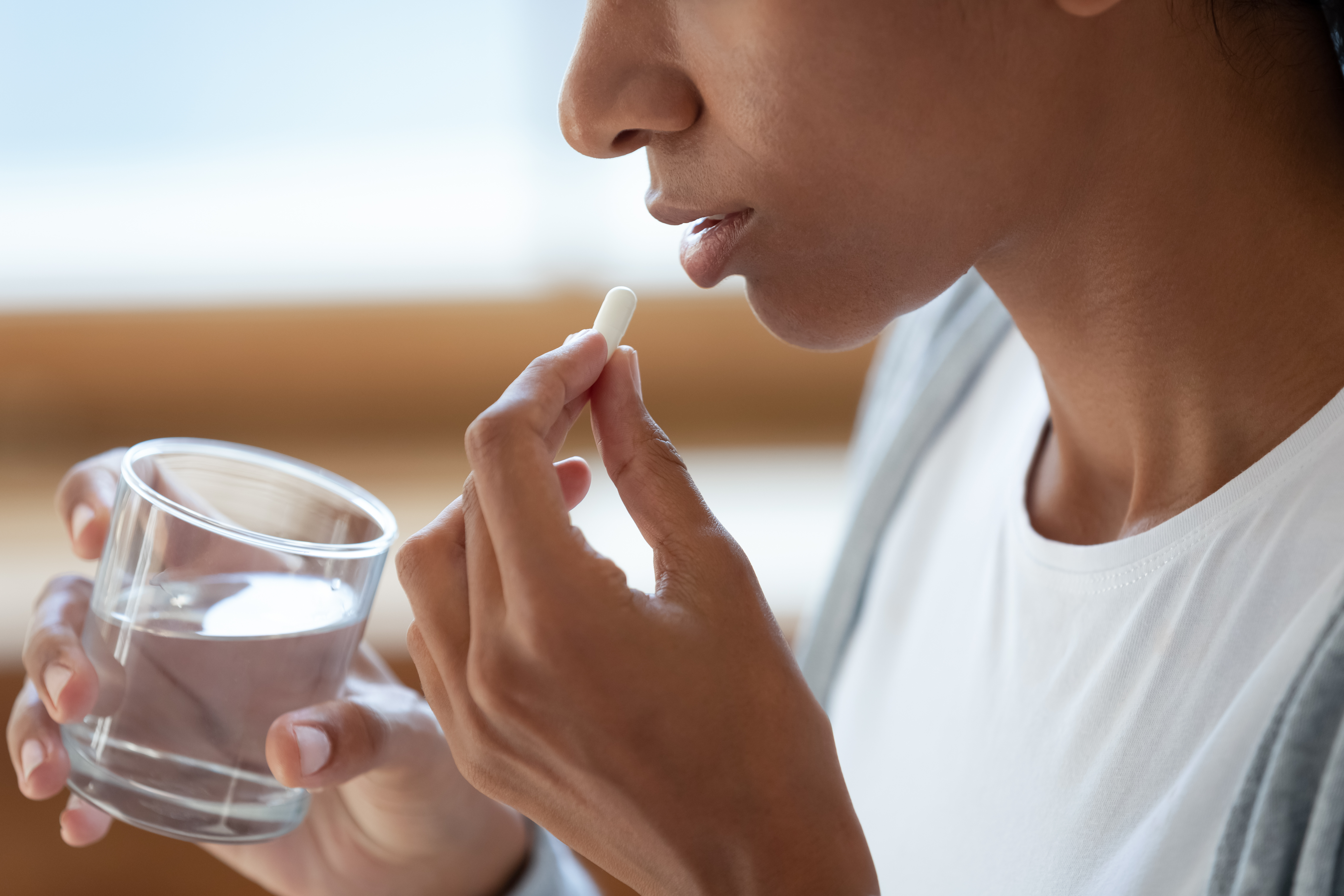 Close up of girl hold glass of water and white pills at her mouth.